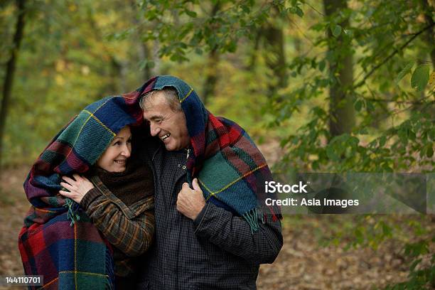 Foto de Sênior Casal Abraçando Sob O Cobertor Na Floresta e mais fotos de stock de 50-54 anos - 50-54 anos, 60-64 anos, Abraçar