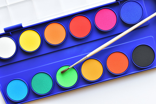 Colorful watercolor paints and fine paint brush in blue box on white background close up, flat lay top view from above