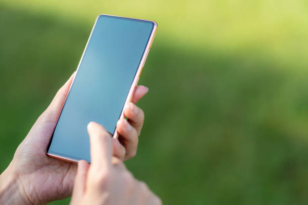 istock Woman's hand holding a smartphone against nature green background 1441112360