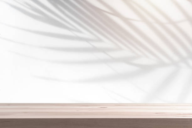 istock Empty wooden table with shadow of tropical leaves on background with copy space 1441115267