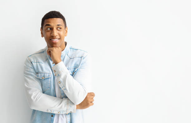 istock Young African American male student smiling joyfully standing on white background looking away. Afro man in casual clothes with happy smile, copy space 1441118640