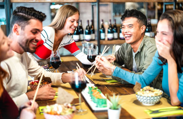 Multicultural trendy friends eating sushi with chopsticks at fusion restaurant bar - Food and beverage life style concept with happy young people having fun together at cool eatery - Vivid filter stock photo