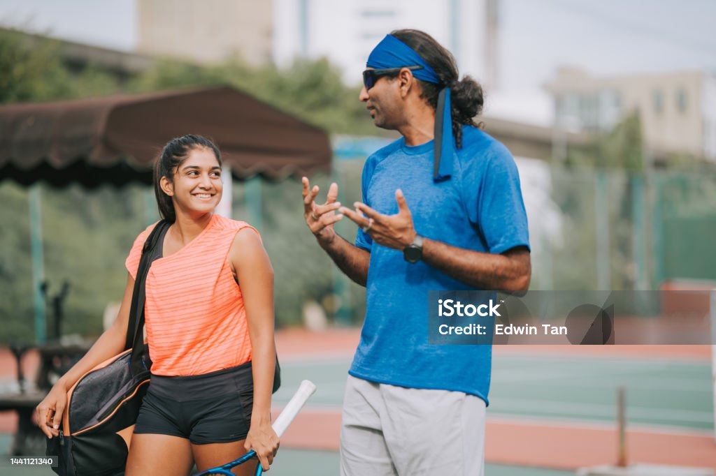 Asian Indian Coach talking to female adult student leaving after practicing in tennis hardcourt Mentorship Stock Photo