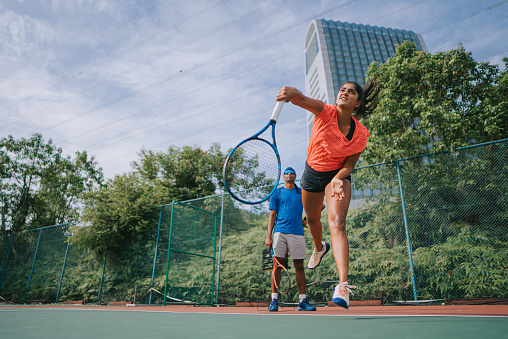 sport training Asian Indian female Tennis Player Serving The Ball practicing at tennis court with coach guidance