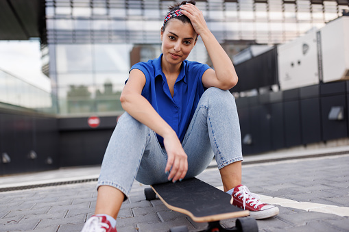 One beautiful young woman sitting on skateboard in the city on sunny day