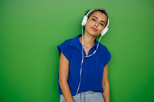 Portrait of young woman with white headphones listening to music on green background