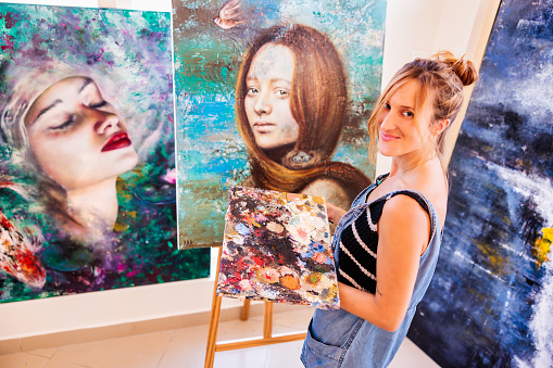 Talented artist smiling at the camera for a photograph with her paintings
