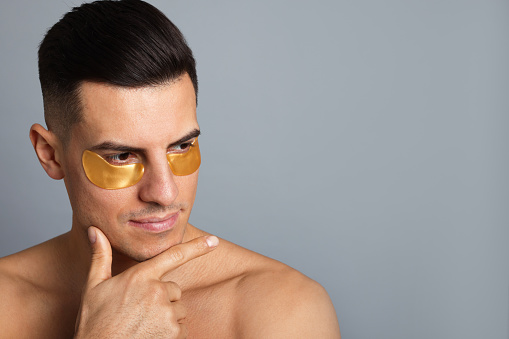 Man with golden under eye patches on grey background. Space for text