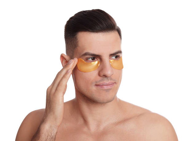 istock Man applying golden under eye patch on white background 1441125702