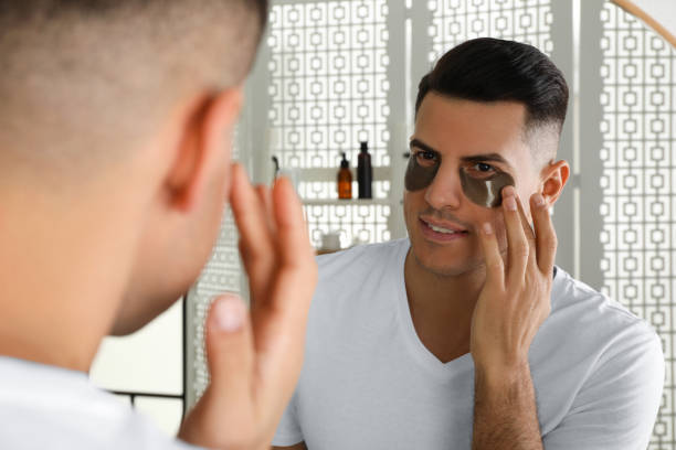 istock Man applying dark under eye patch near mirror at home 1441126229