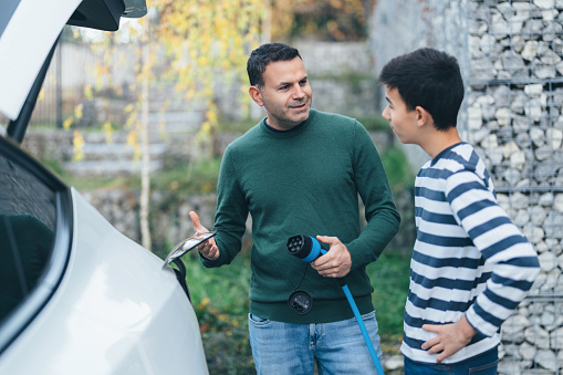 Man showing his son how to charge an electric car