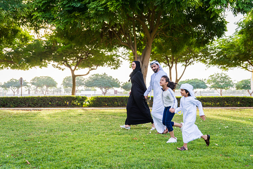 Happy middle-eastern family having fun in a park in Dubai - Parents and kids celebrating the weekend in the nature