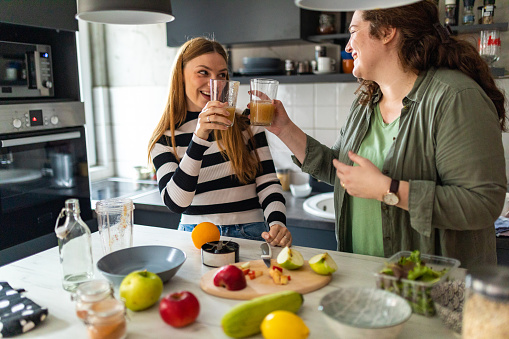 Two female friends drinking smoothie in kitchen at home