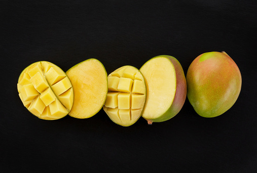 Close up of fresh ripe mango fruits, whole and sliced, mango cubes on a black slate background. Mango. Top view