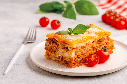 Traditional lasagna with bolognese sauce topped with basil leaves served on a white plate