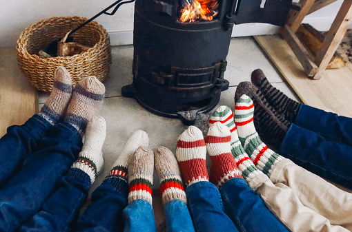 Cropped photo of big family wearing warm woolen socks resting by fireplace together in winter time. Mother, father and children lying on floor warming feet near potbelly stove in country house