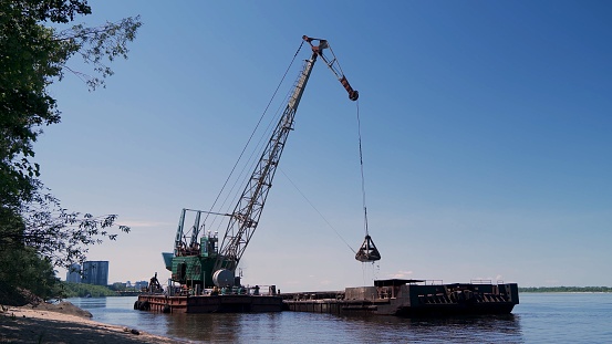 View of a floating crane unloading sand from a moored barge.
