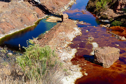 View of Mining activity in Minas de Riotinto in Spain. Polluted river, red and green color of water. Apocalypse scenery. Extractivism. Mining village in Andalusia. Earth and destruction of nature. Extracting natural resources from the Earth to sell on the world market. Ecological disaster. Climate change. Climate change. Water and river pollution. Arid Climate