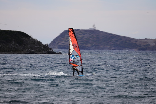 Bodrum, Mugla, Turkey : 23 September 2022: With the end of the summer months, when the population of the popular holiday resort Bodrum decreased, the sea was left to amateur athletes. With the increase in the wind, an amateur man who rents windsurfing from water sports is moving quickly with the waves in the Aegean Sea.