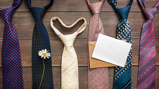 Many different multicolored neckties on a wooden background with chamomile and an empty white sheet for text. Fathers day Wedding Happy birthday concept
