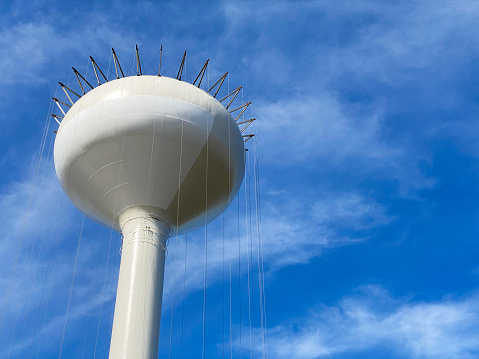 Close up of newly constructed metal water tower being painted against blue sky with clouds