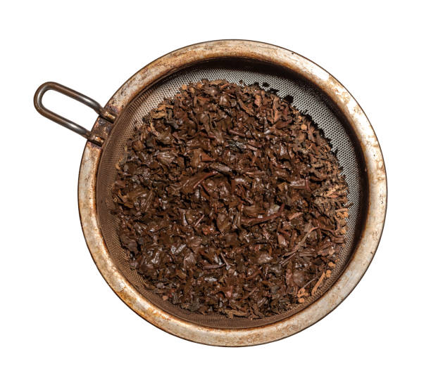 brewed wet tea leaves in a metal strainer, isolated against a white background stock photo