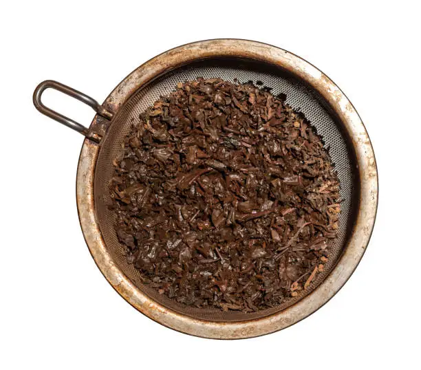 brewed wet tea leaves in a metal strainer, isolated against a white background
