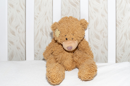 Teddy bear in a white crib, close-up. Children's toys, expectation and birth of a child.