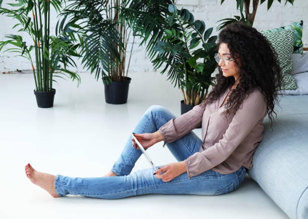 istock Beautiful Afro American female is using a digital tablet while sitting on the floor. 1441154533