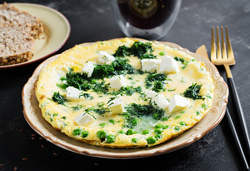 Healthy breakfast. Omelet with green peas, feta cheese and dill. Dark background.