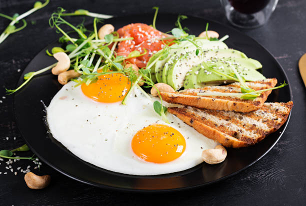 colazione con dieta chetogenica. uova fritte, salmone salato con microgreens, avocado, anacardi e toast cheto. pranzo keto. - appetizer bread breakfast cashew foto e immagini stock