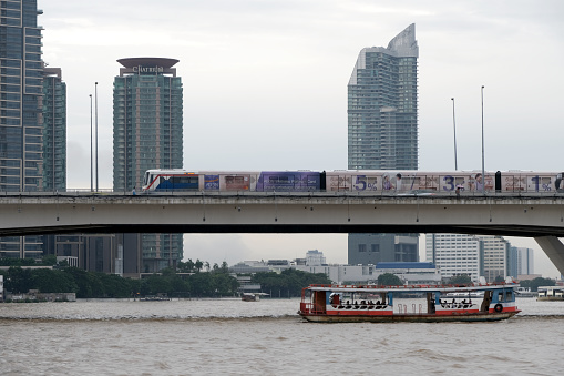 Boat on the Chao Phraya river, Bangkok - Thailand. In the distance the Bts skytrain crossing the river at Saphan taksin.
