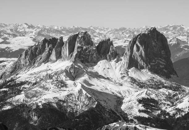 High-key defocused winter landscape featuring the iconic Langkofel peak viewed from a snow-covered observation platform, with two unrecognizable figures experiencing the breathtaking alpine scenery in South Tyrol, Italy.