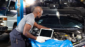 Professional car mechanic repair service and checking car engine by Diagnostics Software computer. Expertise mechanic working in automobile repair garage.