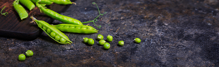 Green peas in pods on a stone surface, horizontal banner, selective focus, low key photography with free copy space for text