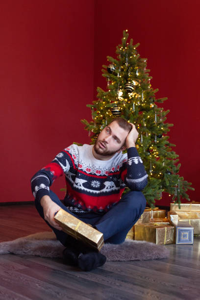istock Man in sweater sits by Christmas tree and thinks about gift 1441164743