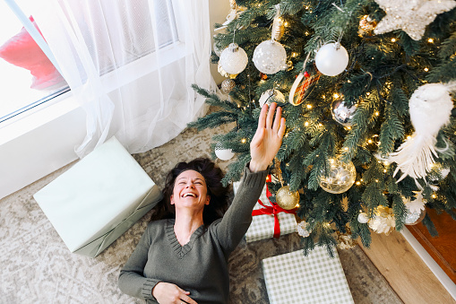 Happy young caucasian woman lying on home floor under decorated christmas tree