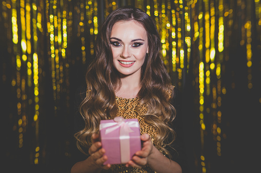 Attractive woman with pink gift present box on golden background