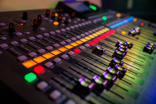 sound mixer with coloured controls and sliders illuminated by stage lights ready for music concert