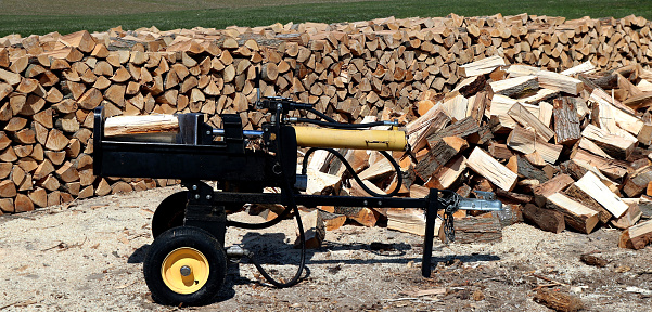 A wood splitter machine with wood logs stacked in a pile background