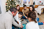 Big family with children sitting on floor playing wooden Scrabble board game at home