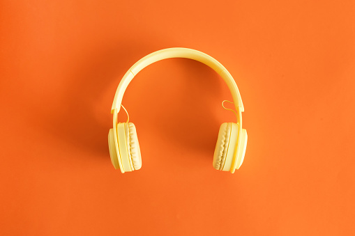 A top view of yellow headphones on a pastel orange background, ntertainment concept