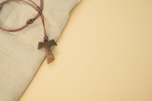 A closeup shot of a wooden tau cross necklace on a wooden background