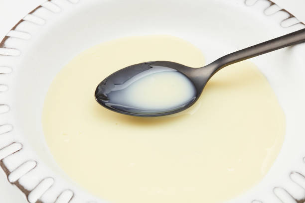 Sweetened condensed milk in a black spoon. Coconut milk in a white plate. Shallow depth of field