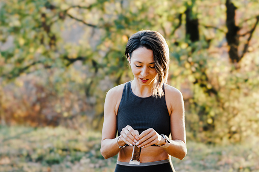 Fit young woman eating power bar during training in nature