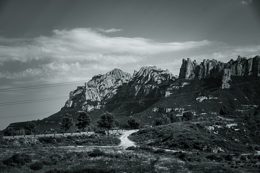 A scenic view of a field and the Montserrat mountain landscape in Spain, grayscale shot