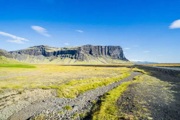 Photo of Landscape of Iceland in the Kalfafell region with stones in grass against a blue sky