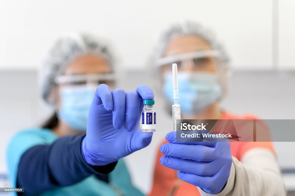 Selective focus image of Two nurses wearing protective masks, holding vaccine and syringe, covid. Closeup, selective focus image of two medical workers holding syringe and vaccine vial. Covid, coronavirus, covid-19 vaccination. Adults Only Stock Photo