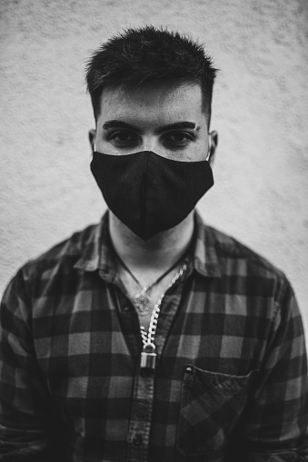 A vertical grayscale shot of a young Spanish man wearing a face mask