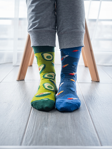 A vertical shot of two different artistic socks on feet, with avocados on the left and blue space on the right